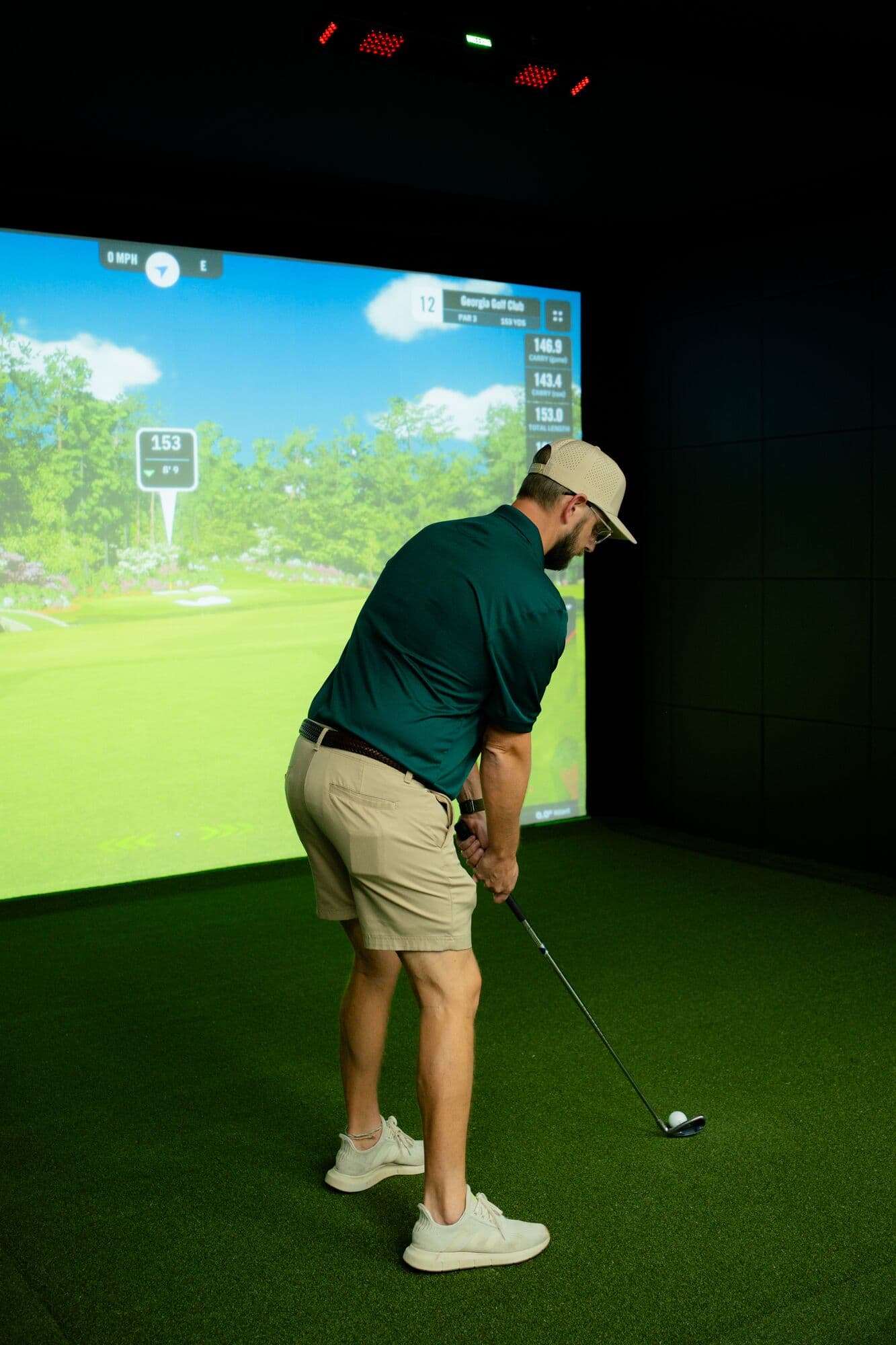 A golfer settling over a driver in front of a Uneekor XO2 simulator screen