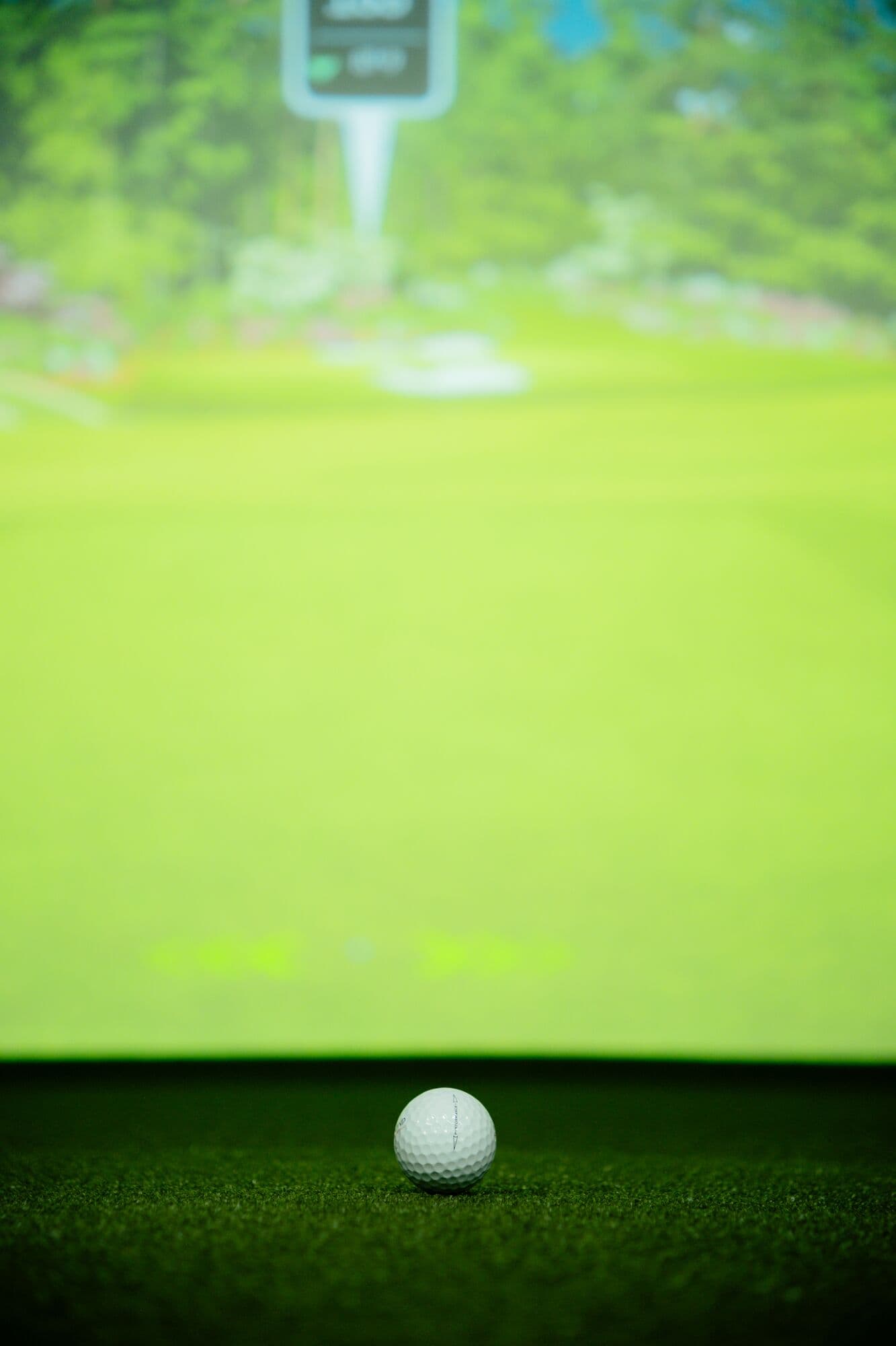 A golf ball on the turf with the simulated fairway glowing behind it