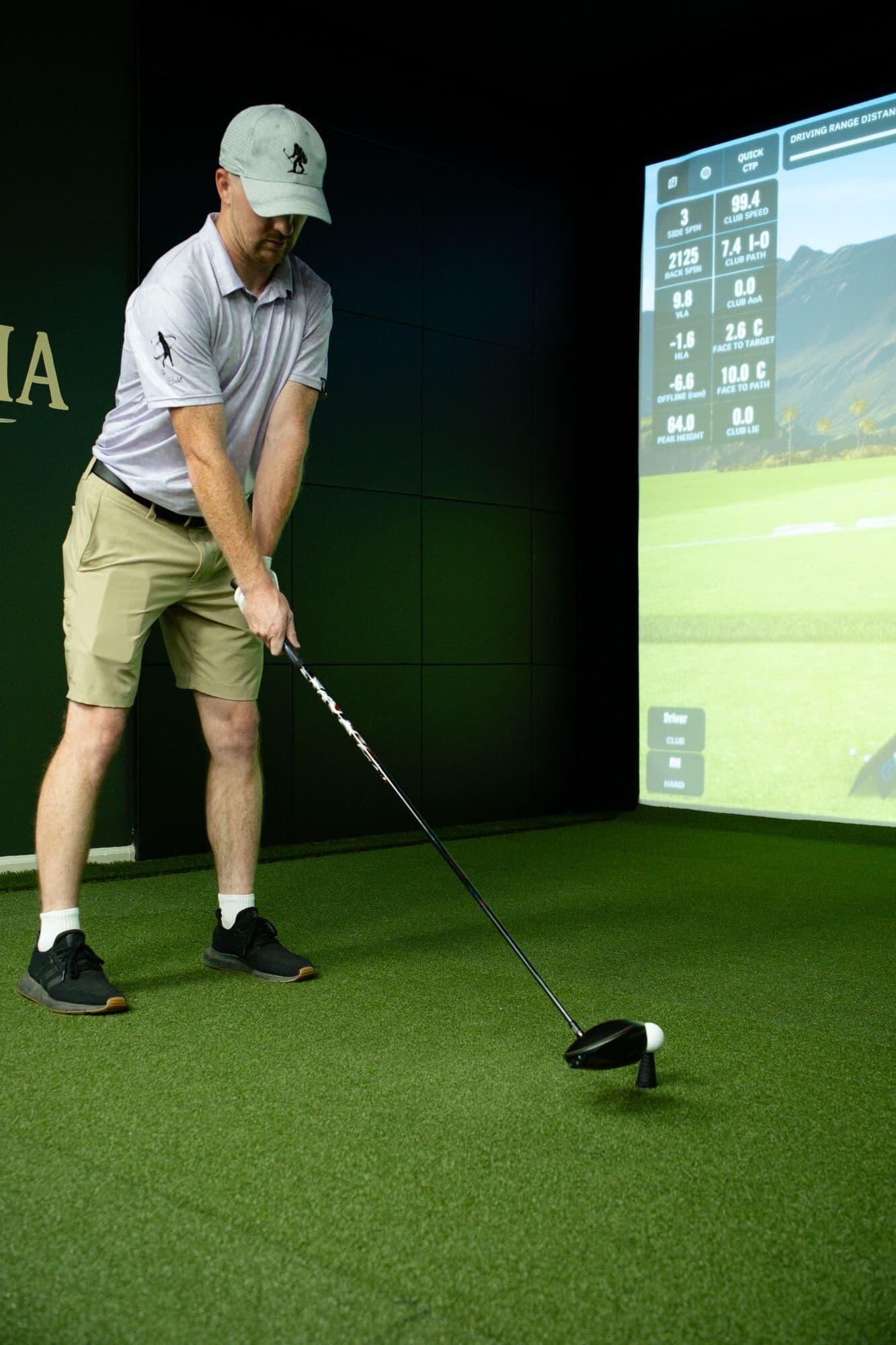 A golfer addressing a driver next to the simulator shot-data display
