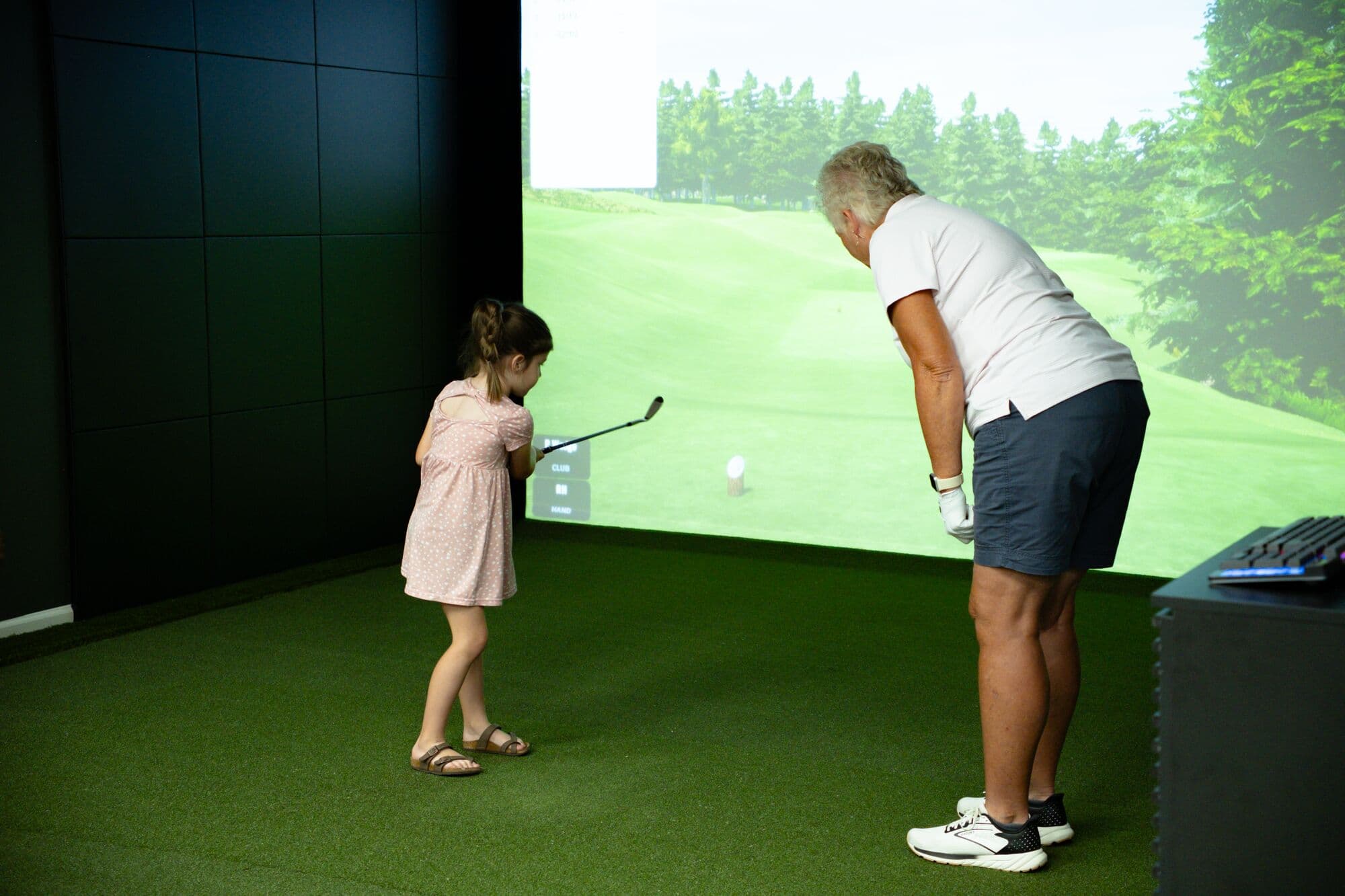 A young girl taking a swing on the simulator with a coach beside her