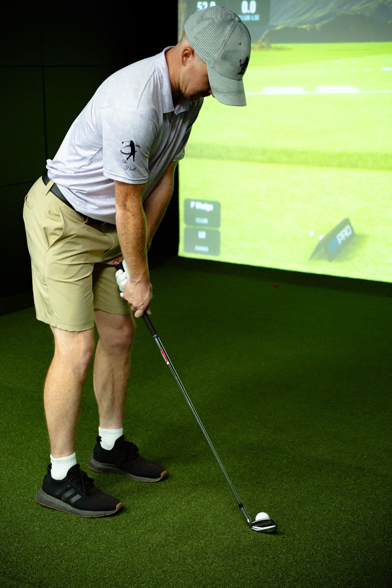 A golfer addressing an iron shot in front of the simulator